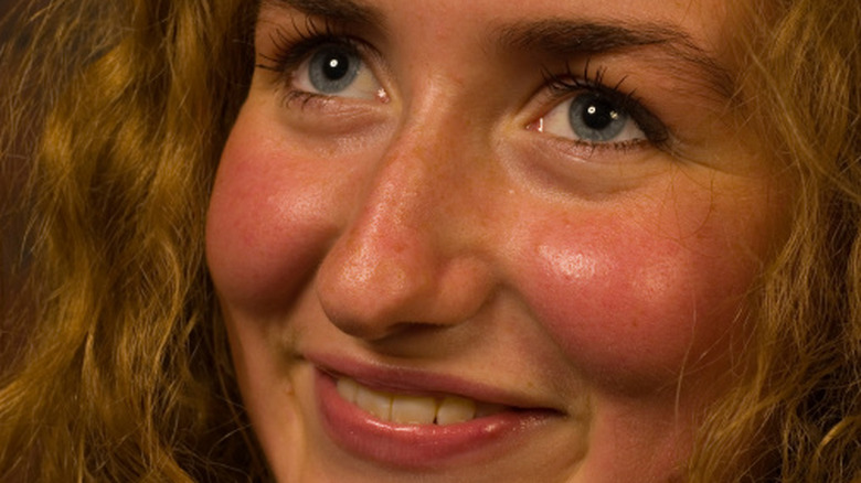 Lächelnde junge blonde Frau mit blauen Augen und roten Wangen