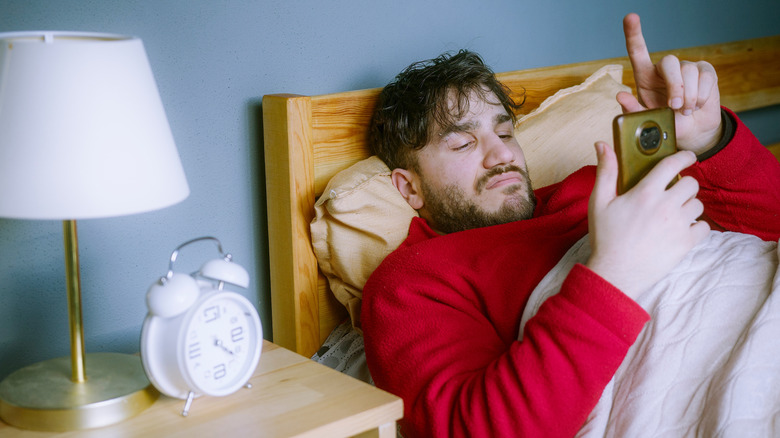 Ein Mann liegt im Bett und scrollt auf seinem Handy.