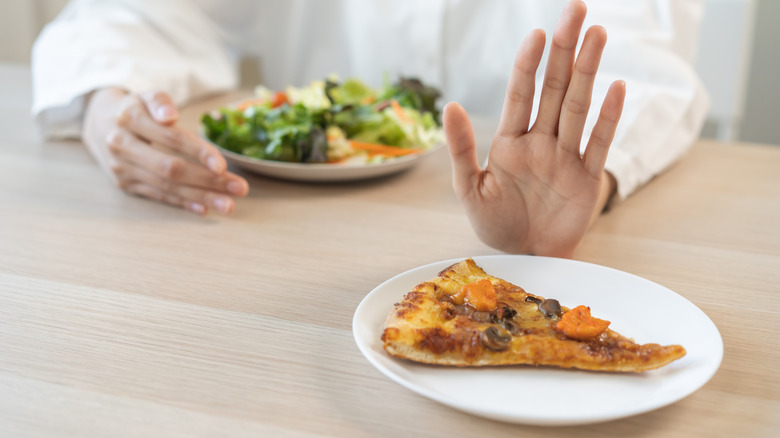 Die Hand schiebt ein Stück Pizza zugunsten des Salats weg